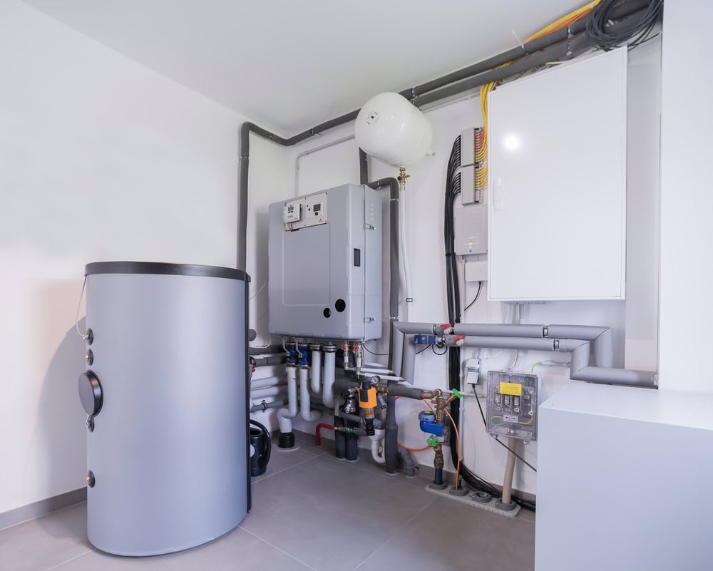 A modern residential boiler room with a hot water tank, various pipes, meters, and heating equipment installed neatly against a white wall on a tiled floor by an expert HVAC contractor in San Mateo County, CA.