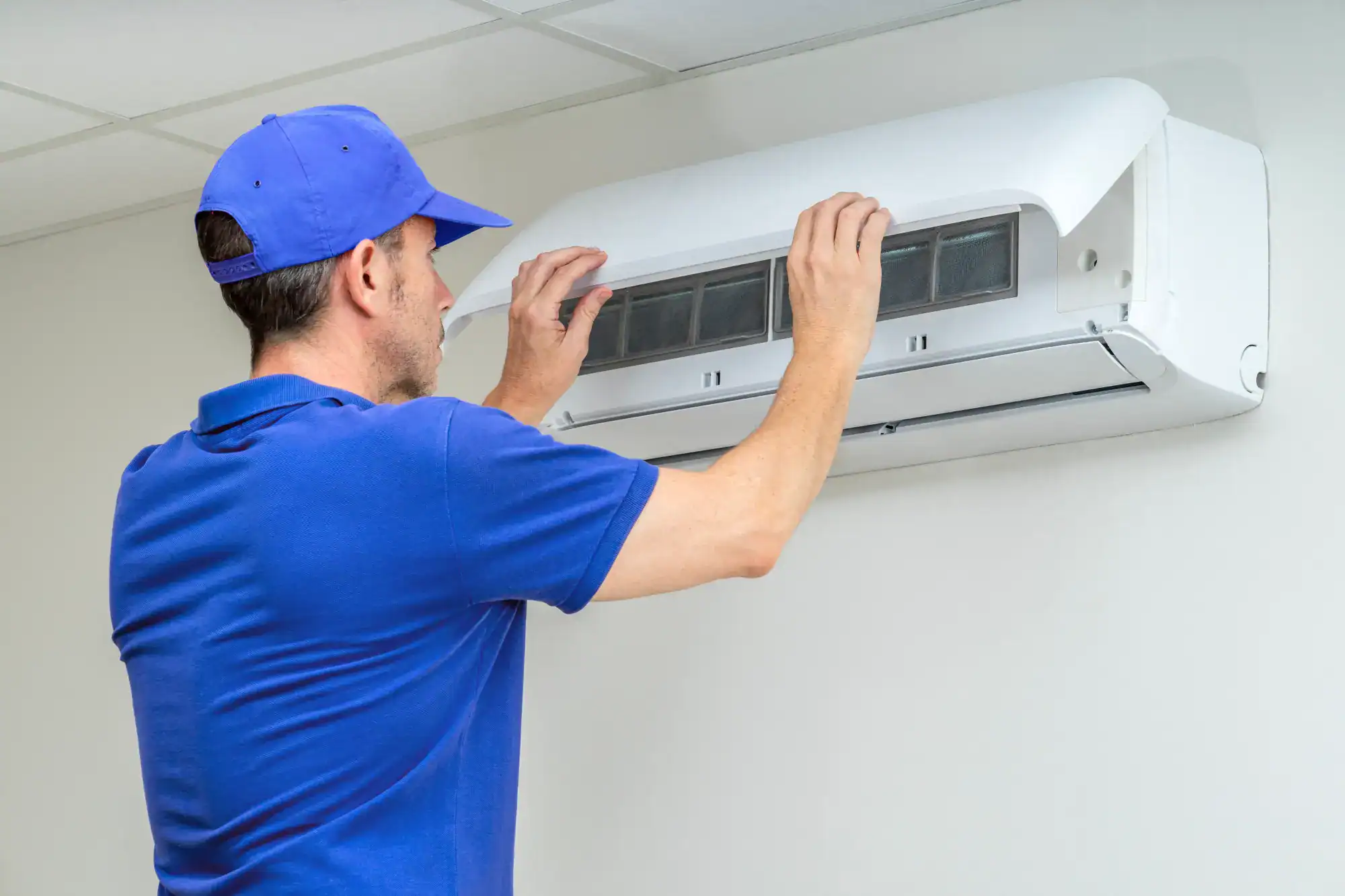 A man in blue shirt fixing an air conditioner.