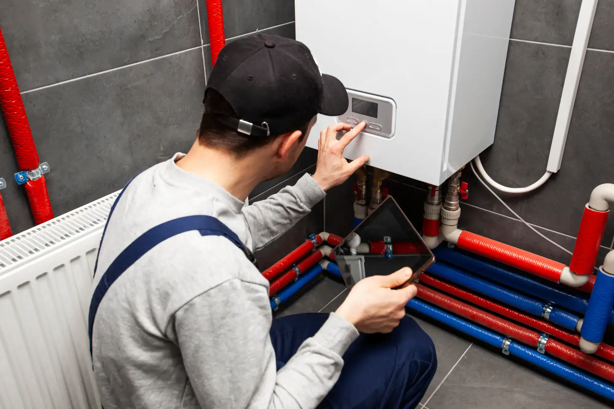 A man in a cap and overalls is working on a gas boiler.