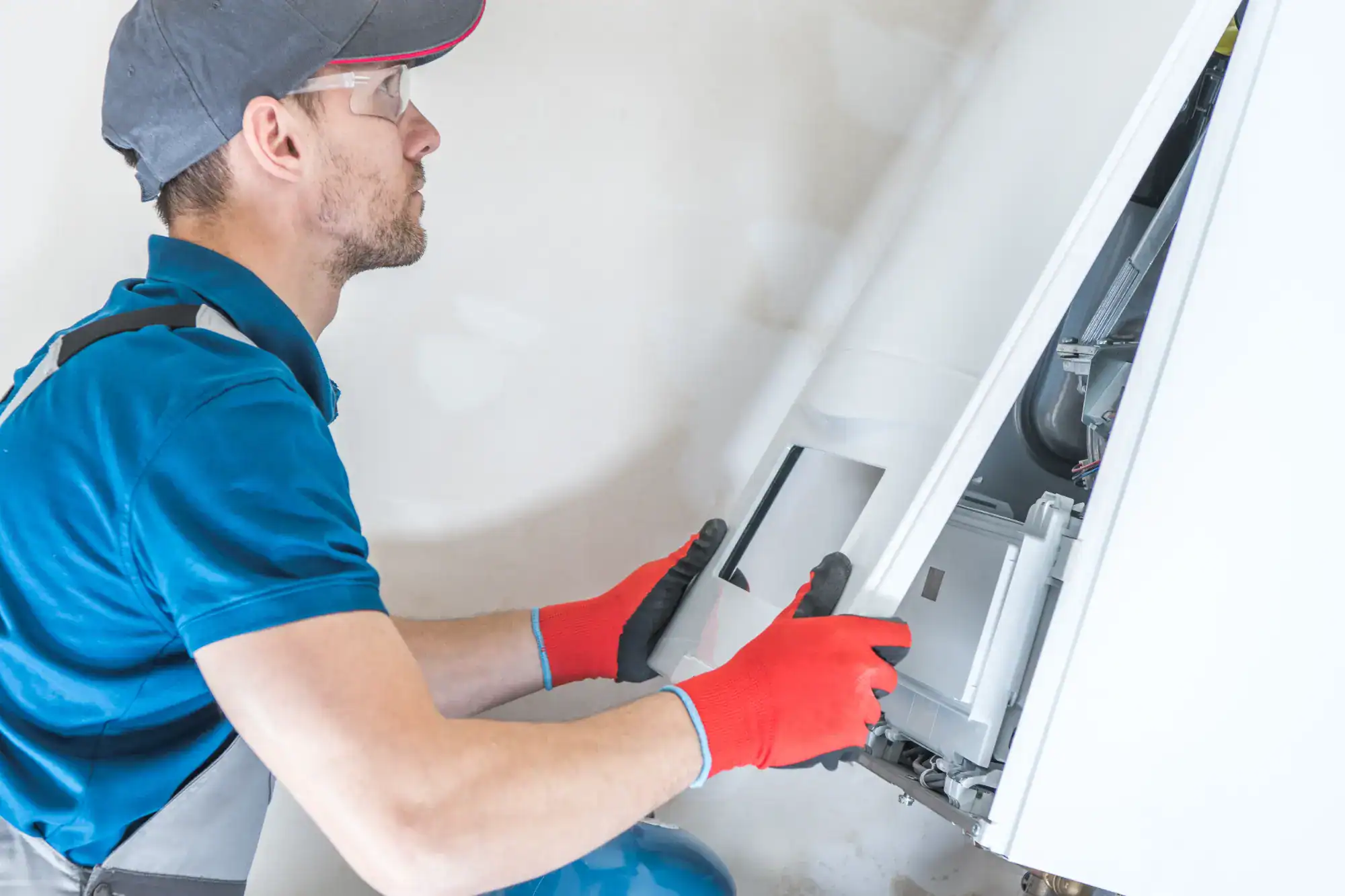 A man in a blue shirt and red gloves is fixing a gas boiler.